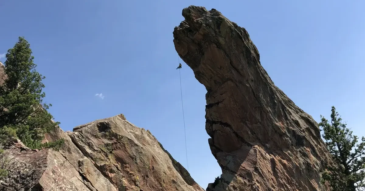 A rock climber rappelling off the Maiden in Boulder Colorado