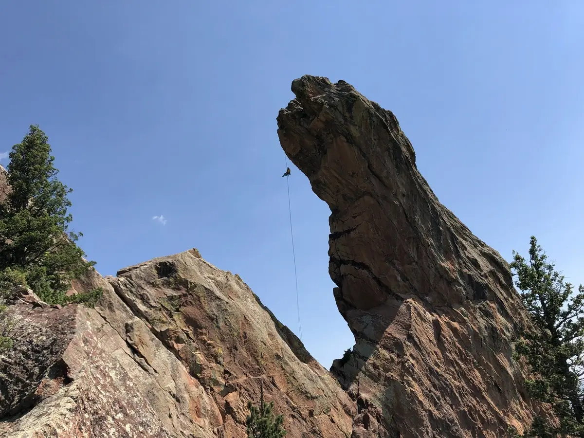 A rock climber rappelling off the Maiden in Boulder Colorado