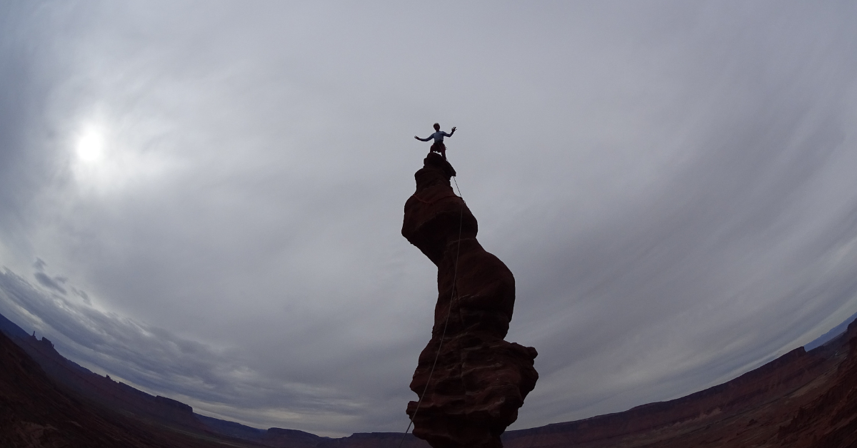 A rock climber stands on top of Ancient Art outside of Moab Utah