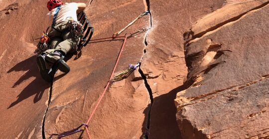 A bigwall climbing course student practicing placing gear while aid climbing in Moab Utah