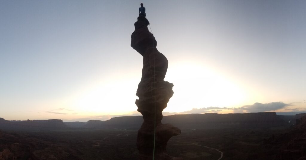 A rock climber on top of Ancient Art in Moab Utah