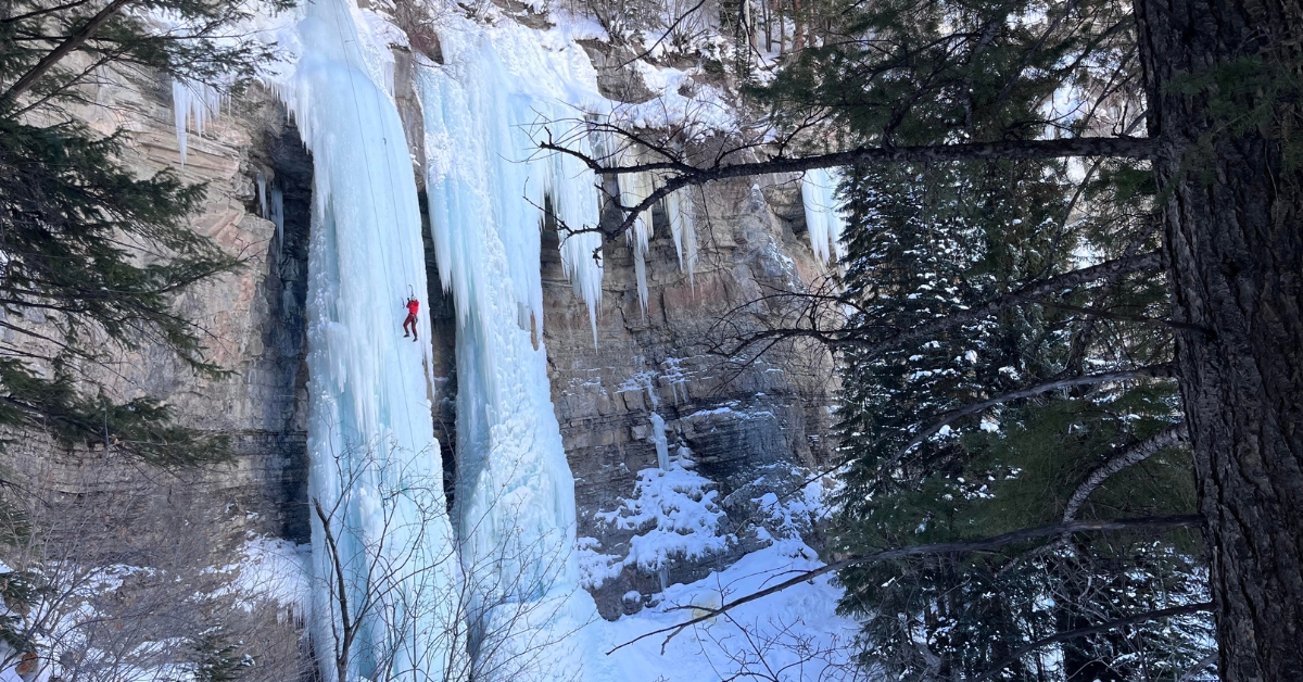 A climber using ice climbing equipment on an ice route in Vail, Colorado, carefully navigating rock and ice with specialized gear.