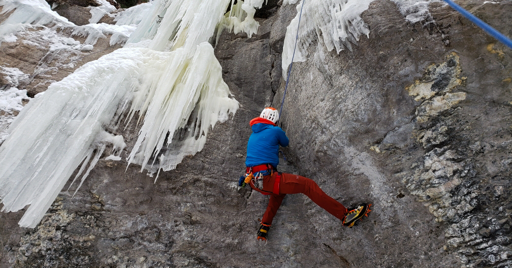 A climber using dry tooling techniques on a mixed route in Vail, Colorado, carefully navigating rock and ice with specialized gear.
