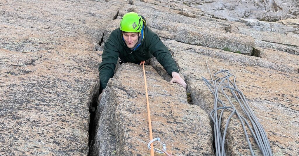 A rock climber in a green helmet jamming cracks on the Diamond Face in Estes Park